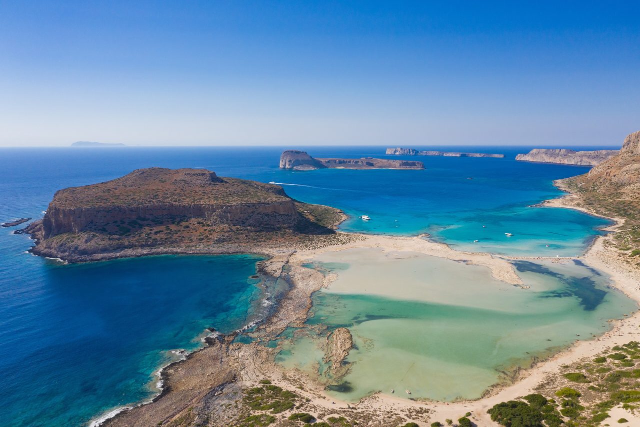 Flygbild över Balos-lagunen på nordvästra Kreta med turkost grunt vatten, ljus sand och klippiga uddar
