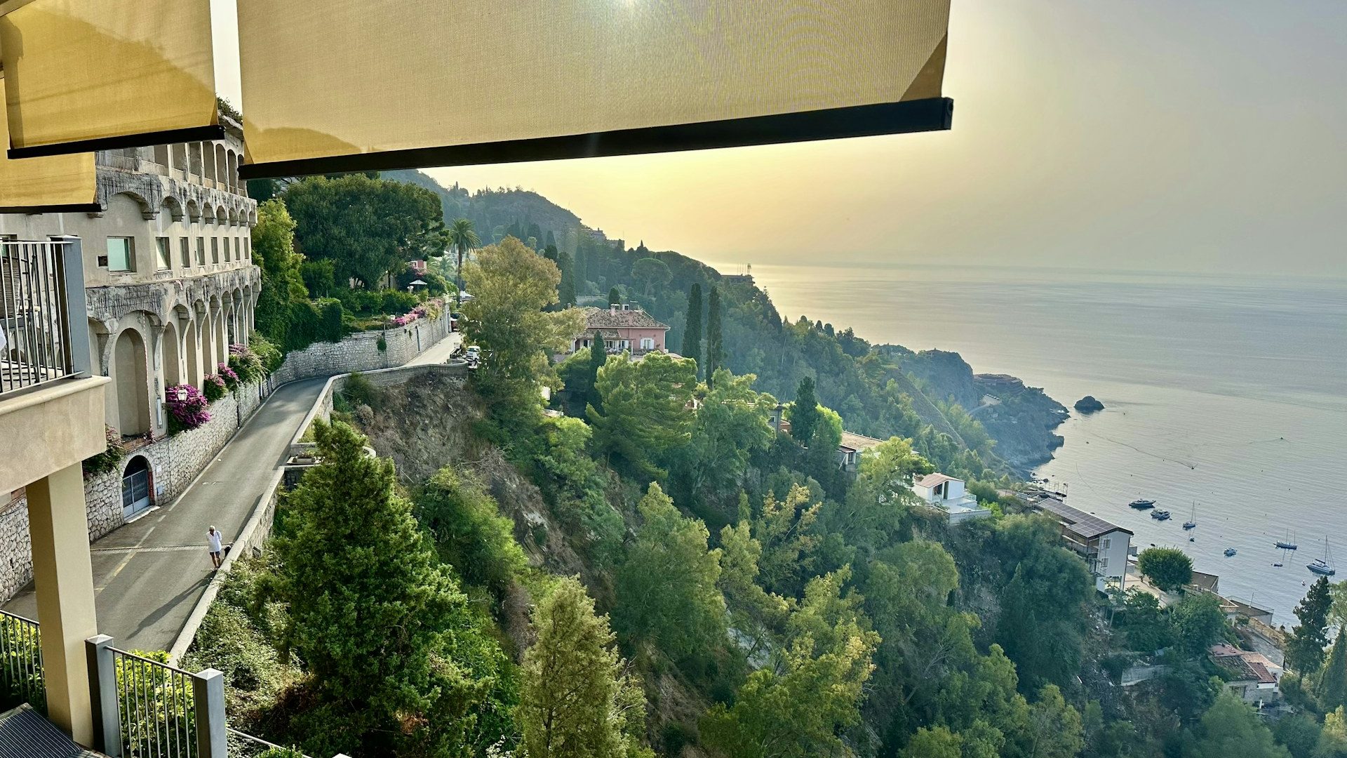 Balkong i Taormina med utsikt över grön kustremsa och havet i gyllene ljus